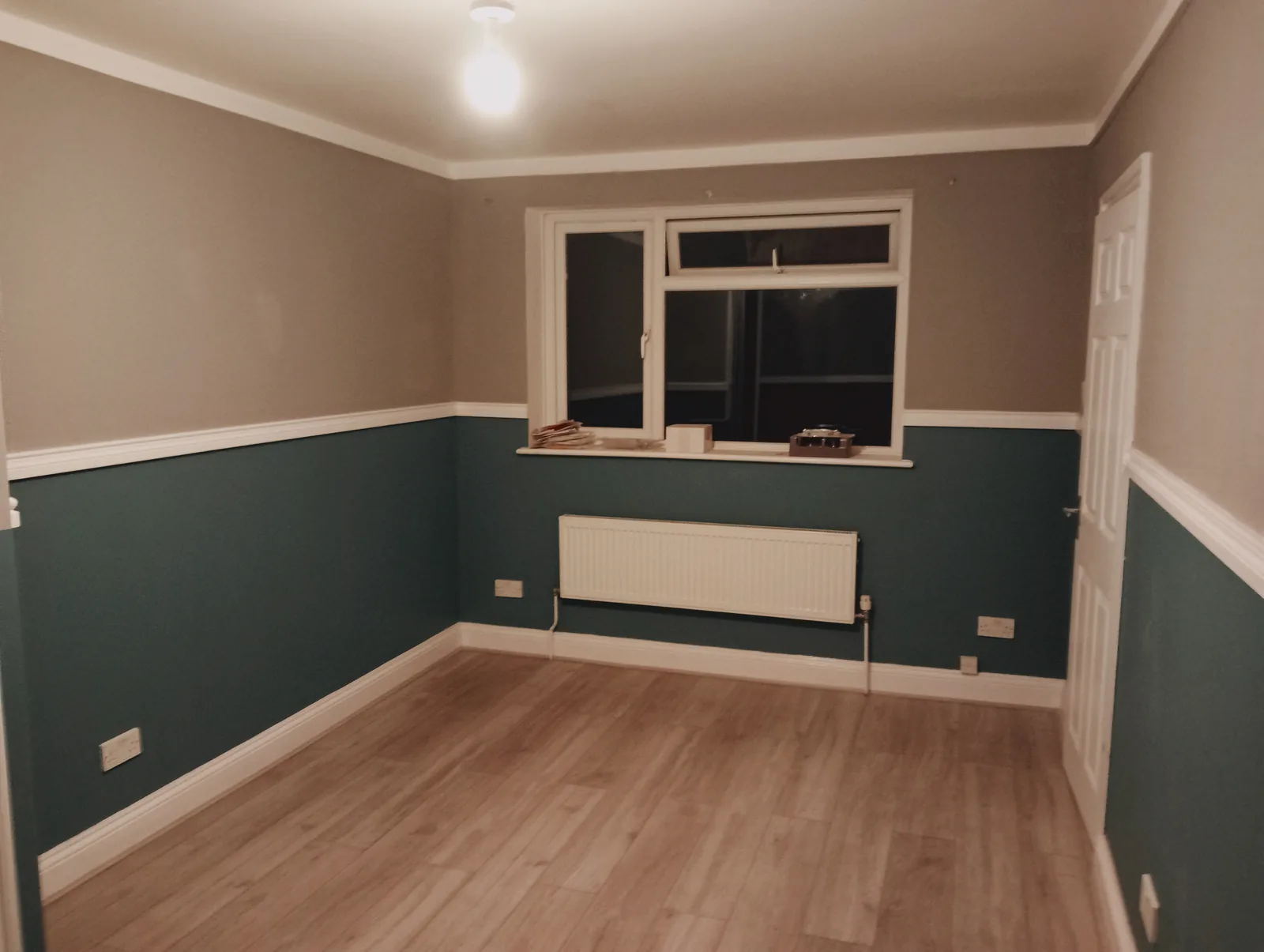 A finished, freshly decorated room with teal panelled walls and a wood-effect floor